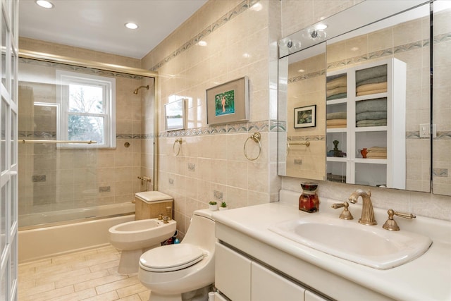 full bathroom with shower / bath combination with glass door, vanity, tile walls, toilet, and a bidet