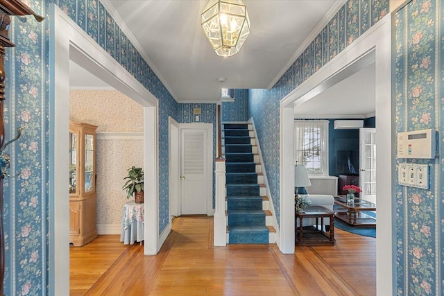 entryway with a wall mounted air conditioner, wood-type flooring, a notable chandelier, and ornamental molding