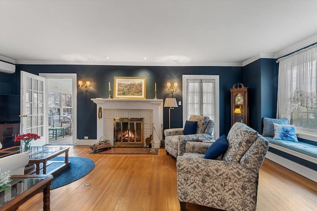 living room with light wood-type flooring, a brick fireplace, crown molding, and a wall unit AC