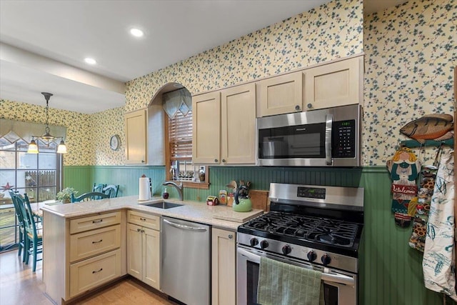 kitchen with cream cabinets, sink, hanging light fixtures, and appliances with stainless steel finishes