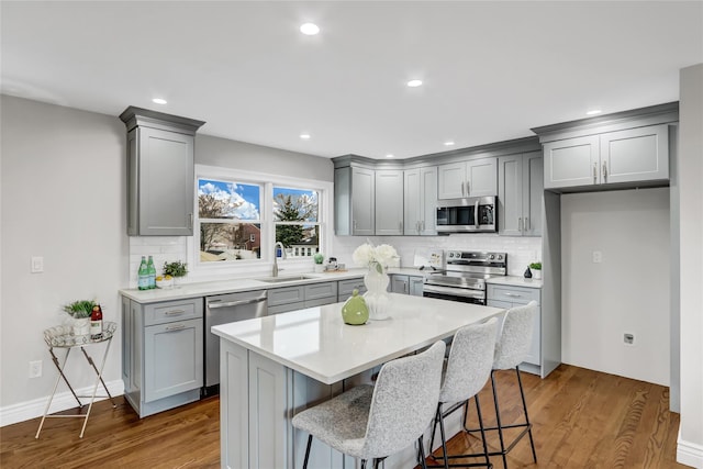 kitchen featuring a breakfast bar, sink, hardwood / wood-style flooring, gray cabinets, and appliances with stainless steel finishes