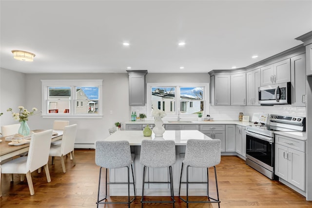 kitchen with gray cabinetry, light hardwood / wood-style flooring, stainless steel appliances, and a baseboard radiator