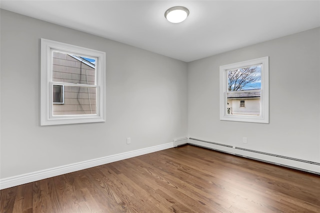 empty room with wood-type flooring, plenty of natural light, and a baseboard heating unit