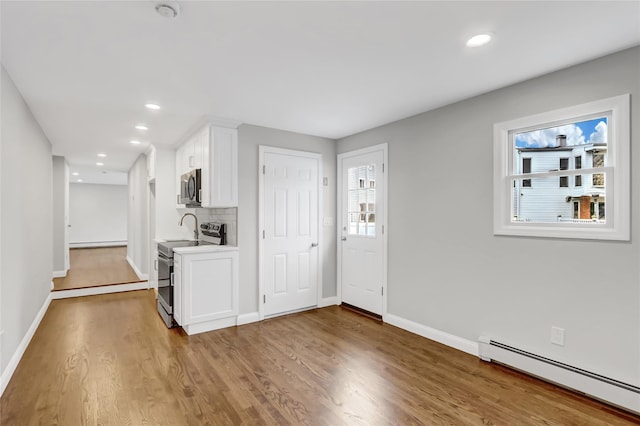 interior space featuring light wood-type flooring, backsplash, stainless steel appliances, baseboard heating, and white cabinets