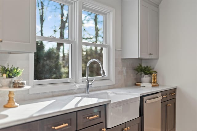 kitchen with light stone countertops, backsplash, stainless steel dishwasher, sink, and white cabinetry