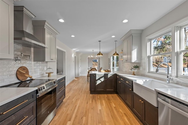 kitchen featuring backsplash, wall chimney exhaust hood, light wood-type flooring, decorative light fixtures, and stainless steel appliances