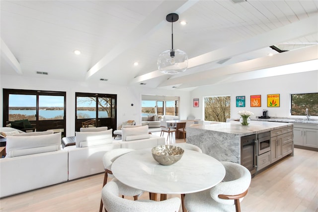 dining room with vaulted ceiling with beams, sink, a water view, and light hardwood / wood-style floors