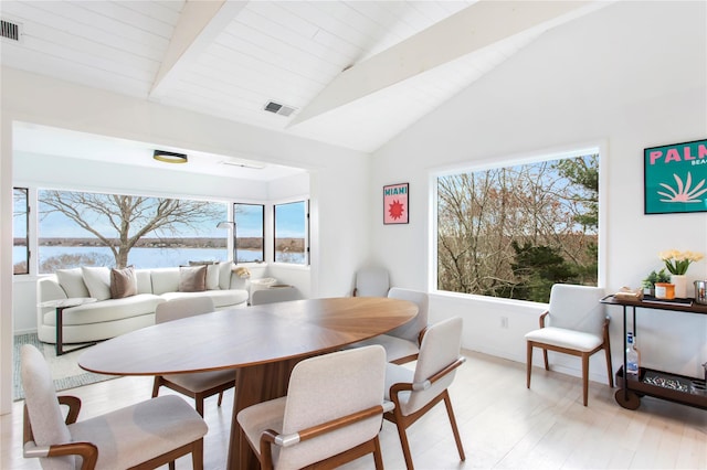 dining area featuring vaulted ceiling with beams, light hardwood / wood-style flooring, and a water view