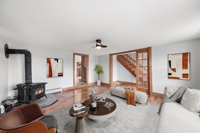 living room featuring baseboard heating, a wood stove, ceiling fan, and wood-type flooring