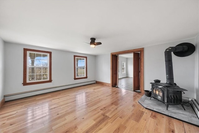 unfurnished living room featuring light wood-type flooring, a wood stove, baseboard heating, and ceiling fan