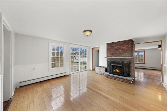 unfurnished living room featuring a fireplace, light hardwood / wood-style flooring, and a baseboard heating unit