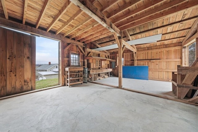 misc room featuring wood walls, a healthy amount of sunlight, concrete flooring, and beam ceiling