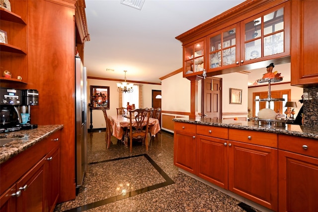 kitchen featuring stainless steel fridge, dark stone counters, crown molding, decorative light fixtures, and an inviting chandelier