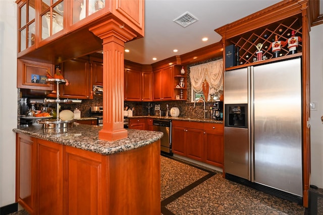 kitchen featuring kitchen peninsula, decorative columns, stainless steel appliances, sink, and dark stone countertops