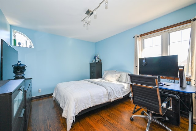 bedroom with rail lighting and dark hardwood / wood-style floors