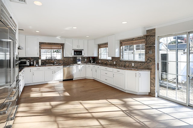 kitchen featuring decorative backsplash, built in microwave, white cabinets, and stainless steel dishwasher