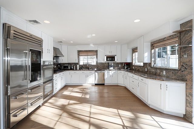 kitchen with built in appliances, extractor fan, decorative backsplash, white cabinets, and light wood-type flooring