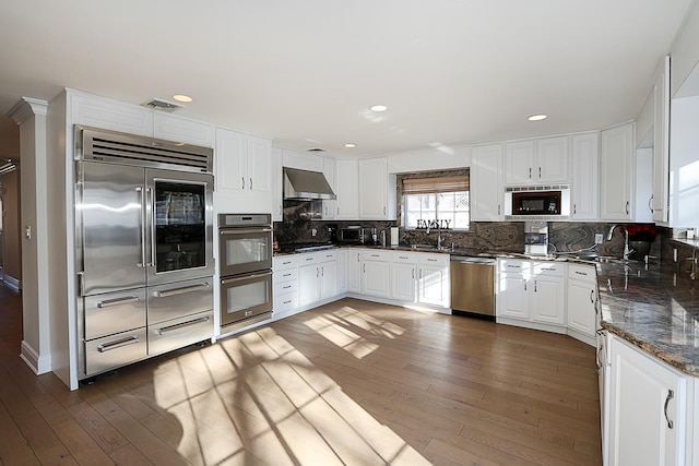 kitchen featuring built in appliances, dark hardwood / wood-style floors, white cabinetry, and wall chimney range hood