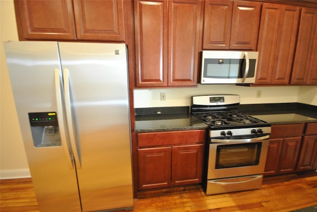 kitchen featuring dark stone countertops, wood-type flooring, and appliances with stainless steel finishes