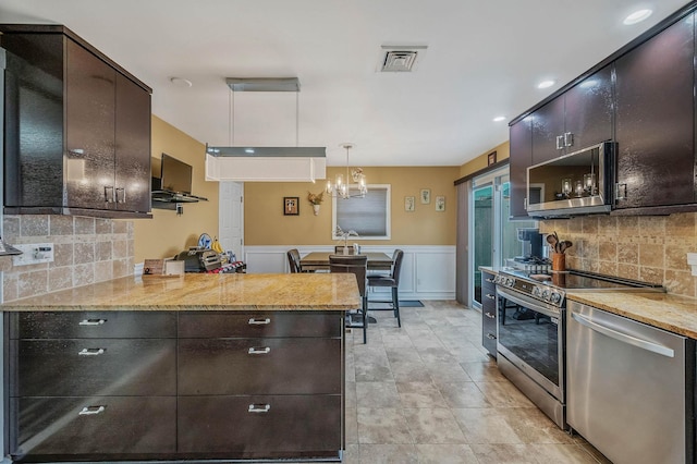 kitchen with kitchen peninsula, hanging light fixtures, appliances with stainless steel finishes, and tasteful backsplash