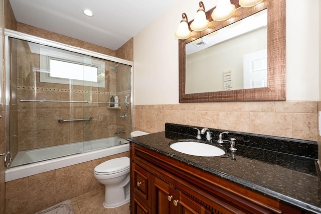 full bathroom with tile patterned flooring, enclosed tub / shower combo, toilet, vanity, and tile walls