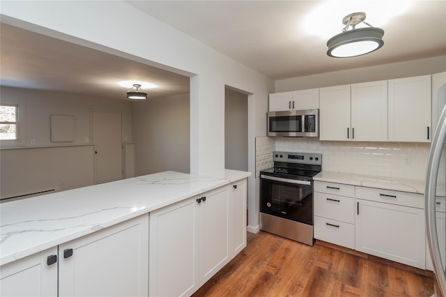 kitchen featuring light stone counters, wood finished floors, white cabinetry, appliances with stainless steel finishes, and decorative backsplash