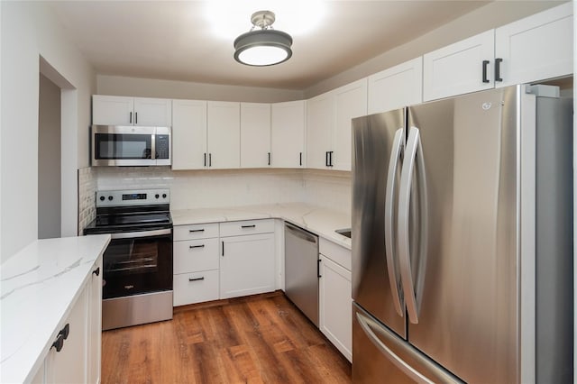 kitchen with appliances with stainless steel finishes, white cabinets, dark wood-style floors, and tasteful backsplash