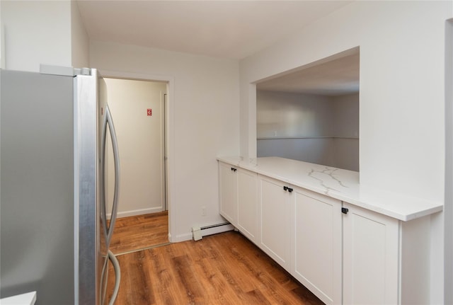 kitchen with a baseboard radiator, freestanding refrigerator, light stone countertops, light wood-type flooring, and white cabinetry