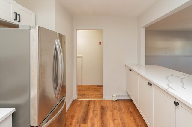 kitchen with light wood finished floors, white cabinets, freestanding refrigerator, light stone countertops, and baseboard heating