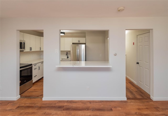 kitchen with appliances with stainless steel finishes, white cabinets, light countertops, and wood finished floors