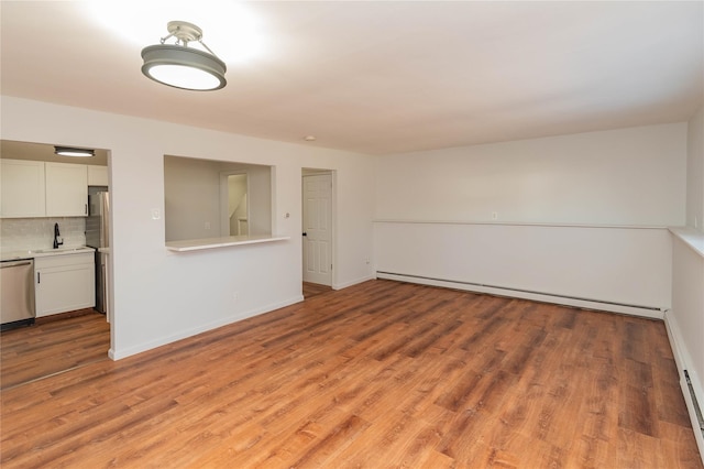 empty room with a baseboard heating unit, baseboards, a sink, and light wood finished floors