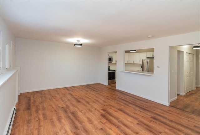 unfurnished living room featuring a baseboard heating unit, baseboards, and wood finished floors