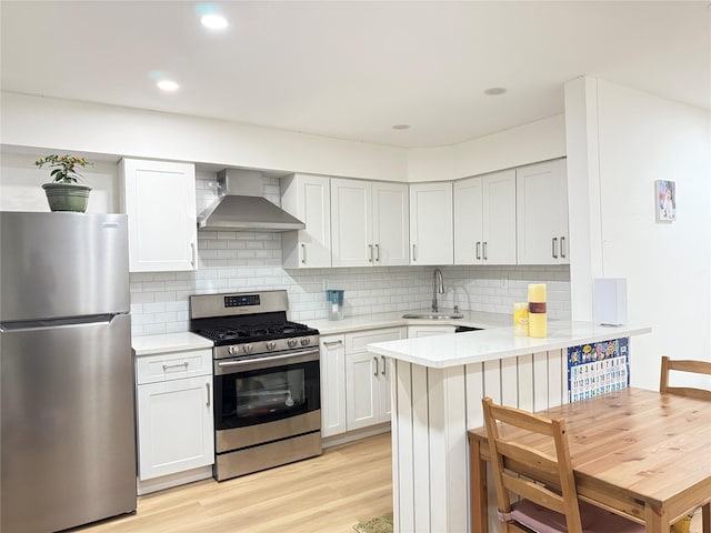 kitchen with kitchen peninsula, appliances with stainless steel finishes, wall chimney exhaust hood, sink, and white cabinets