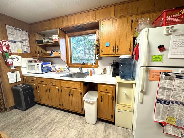 kitchen featuring white appliances, a sink, light countertops, brown cabinetry, and light wood-type flooring