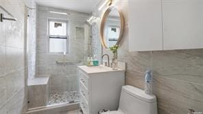 bathroom featuring tiled shower, vanity, tile walls, and toilet