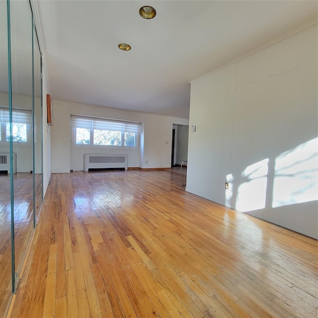 unfurnished living room featuring radiator heating unit, a baseboard radiator, and light wood-type flooring