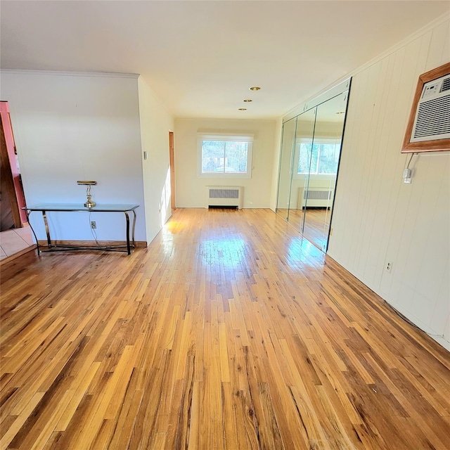 unfurnished living room with a wall mounted air conditioner, radiator heating unit, crown molding, and light hardwood / wood-style flooring