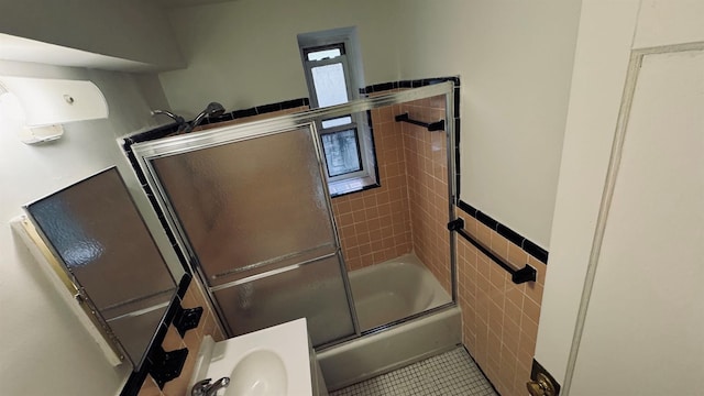 bathroom with tile patterned floors, shower / bath combination with glass door, sink, and tile walls