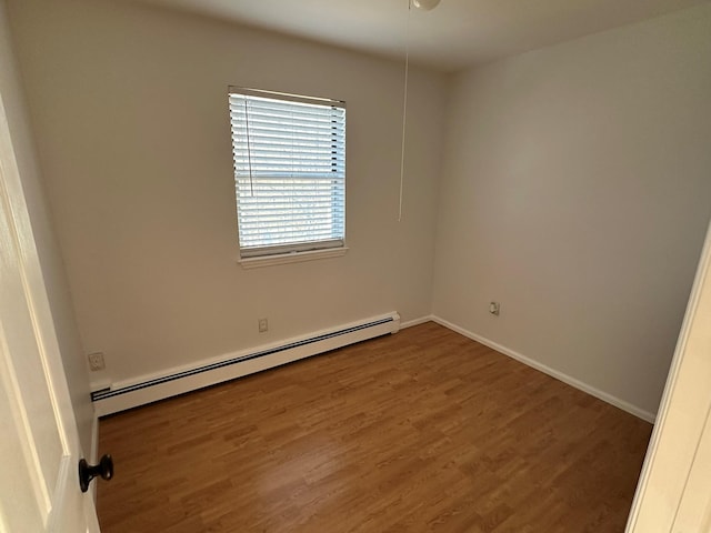 unfurnished room featuring hardwood / wood-style flooring and a baseboard heating unit