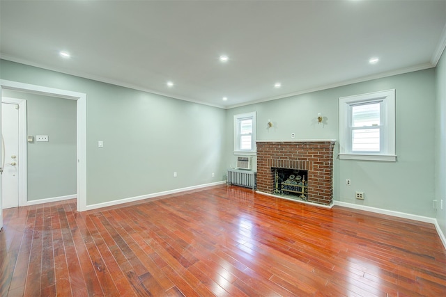 unfurnished living room featuring wood-type flooring, a brick fireplace, a wealth of natural light, and crown molding