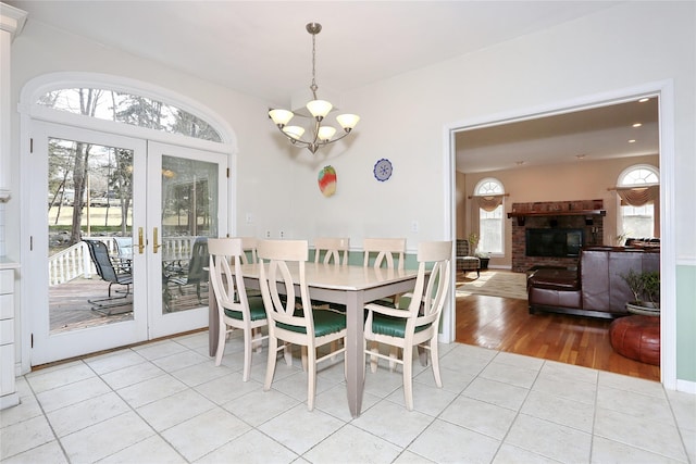 dining room with french doors, a brick fireplace, light tile patterned flooring, and a chandelier