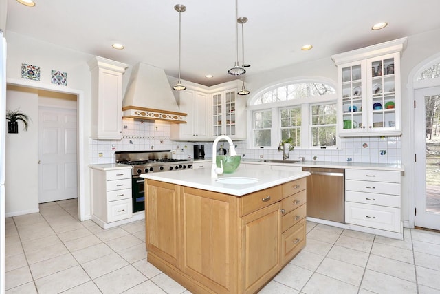 kitchen featuring appliances with stainless steel finishes, a kitchen island with sink, light brown cabinetry, custom range hood, and sink