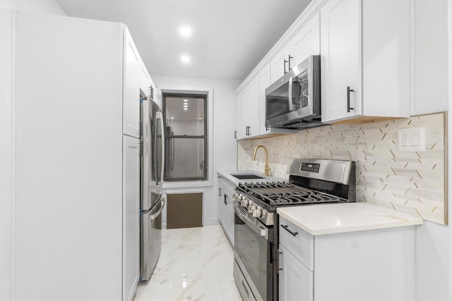 kitchen featuring light stone countertops, decorative backsplash, stainless steel appliances, sink, and white cabinetry