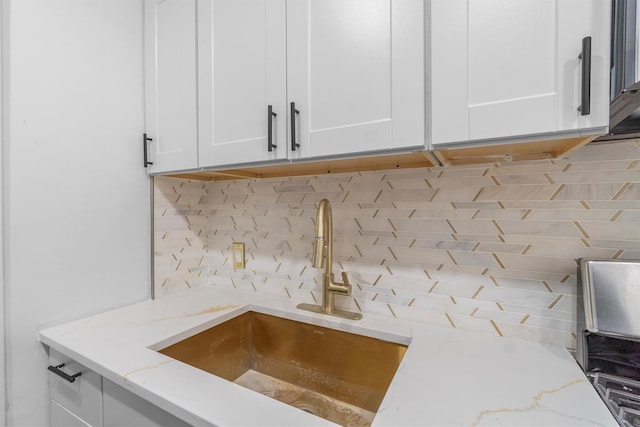 room details with white cabinetry, decorative backsplash, sink, and light stone counters