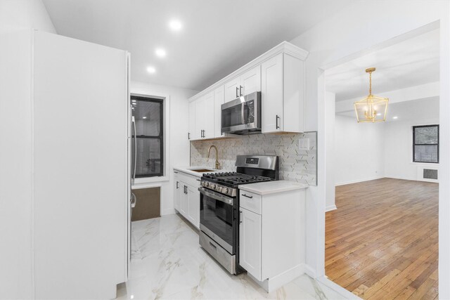 kitchen with appliances with stainless steel finishes, light wood-type flooring, backsplash, sink, and white cabinets