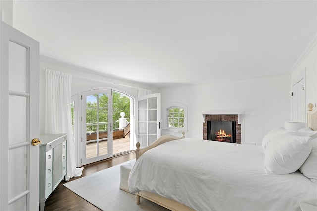 bedroom featuring access to exterior, ornamental molding, a brick fireplace, and dark wood-type flooring