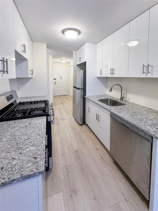 kitchen with white cabinets, sink, appliances with stainless steel finishes, and light hardwood / wood-style flooring