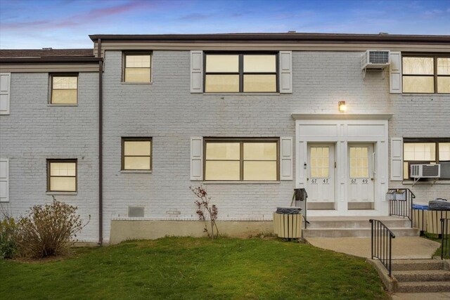 back house at dusk featuring a wall unit AC, cooling unit, and a lawn