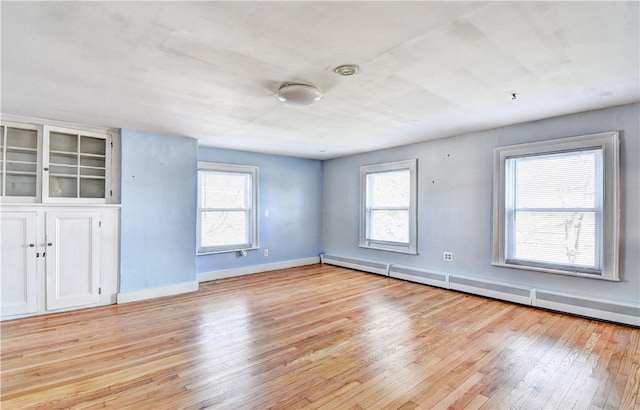 empty room with a healthy amount of sunlight, a baseboard heating unit, and light wood-type flooring