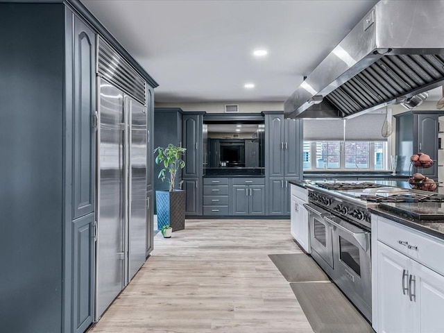 kitchen with light hardwood / wood-style floors, high end appliances, white cabinetry, and range hood